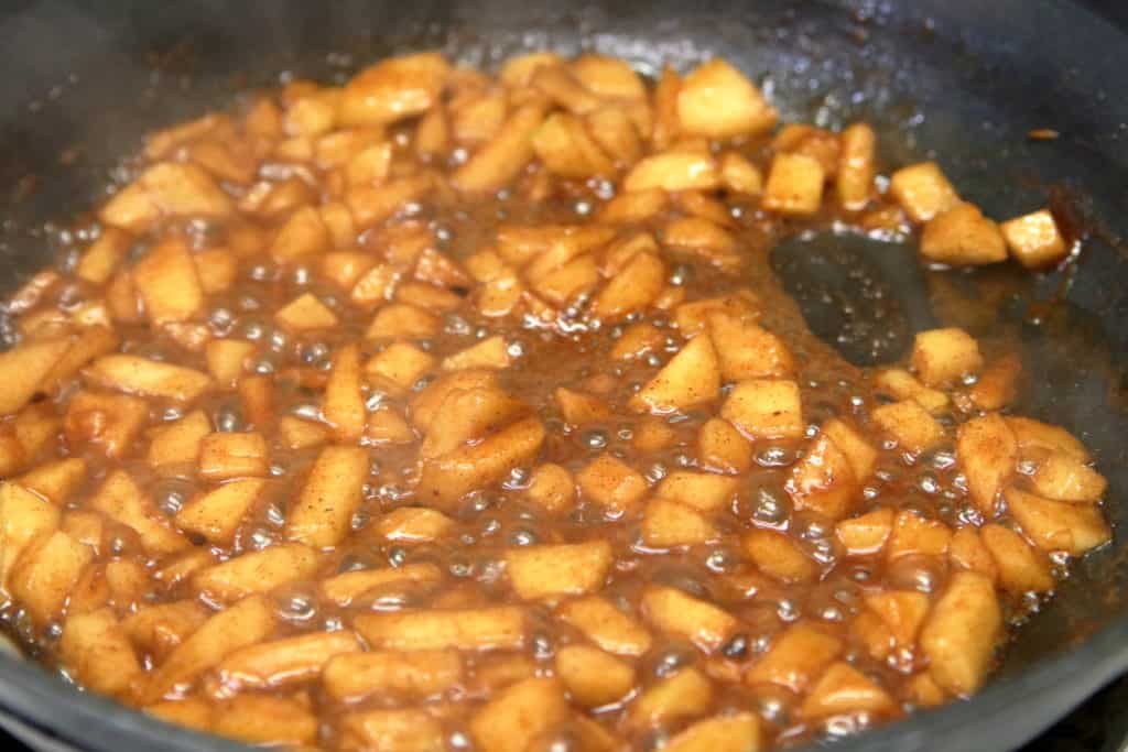 Warm cinnamon apple pie filling in a saute pan simmering in apple cider.
