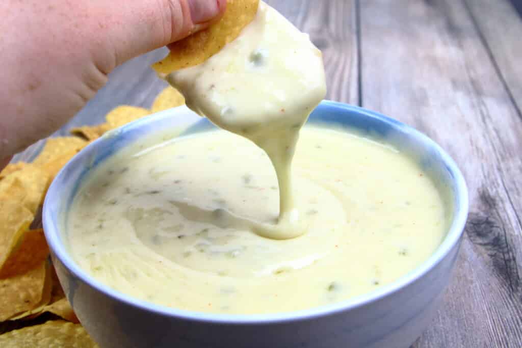 Queso blanco dip dripping from a tortilla chip