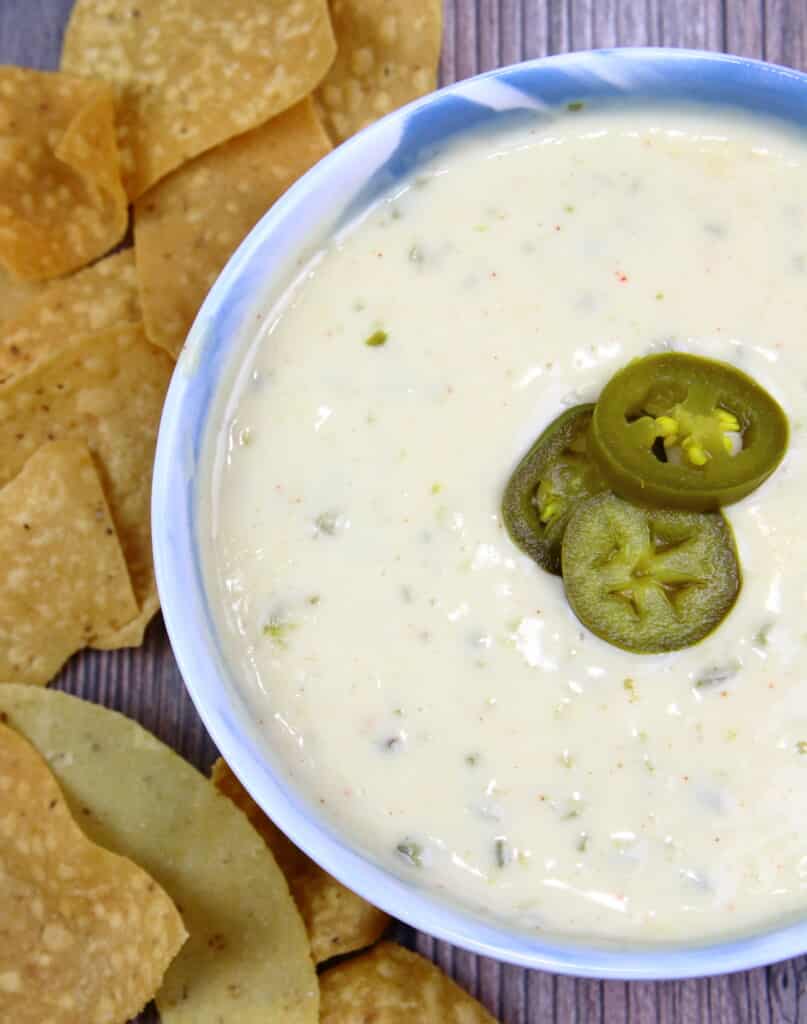 Queso Blanco topped with peppers next to a pile of tortilla chips.