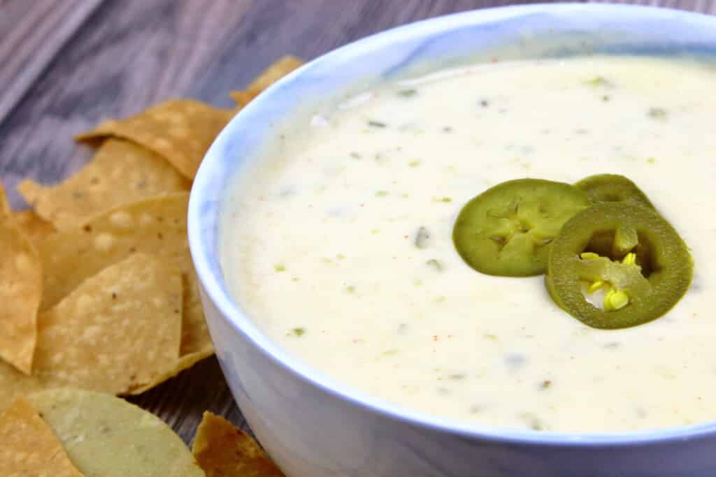 Queso Blanco topped with peppers next to a pile of tortilla chips.