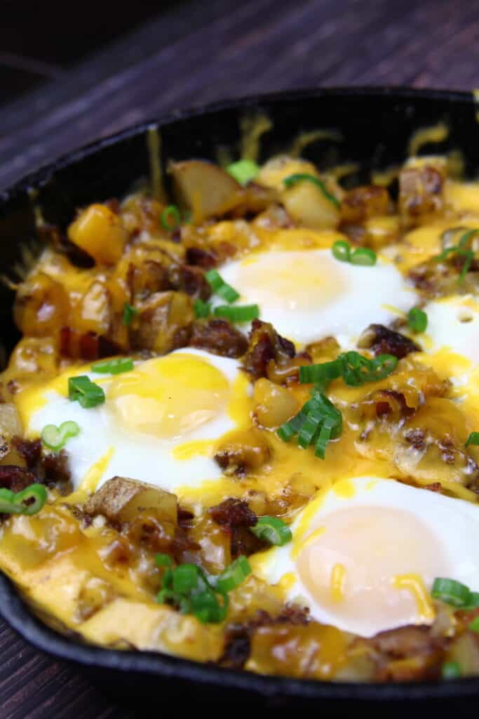 Breakfast Hash with melted cheese, over easy eggs, and potatoes in a skillet