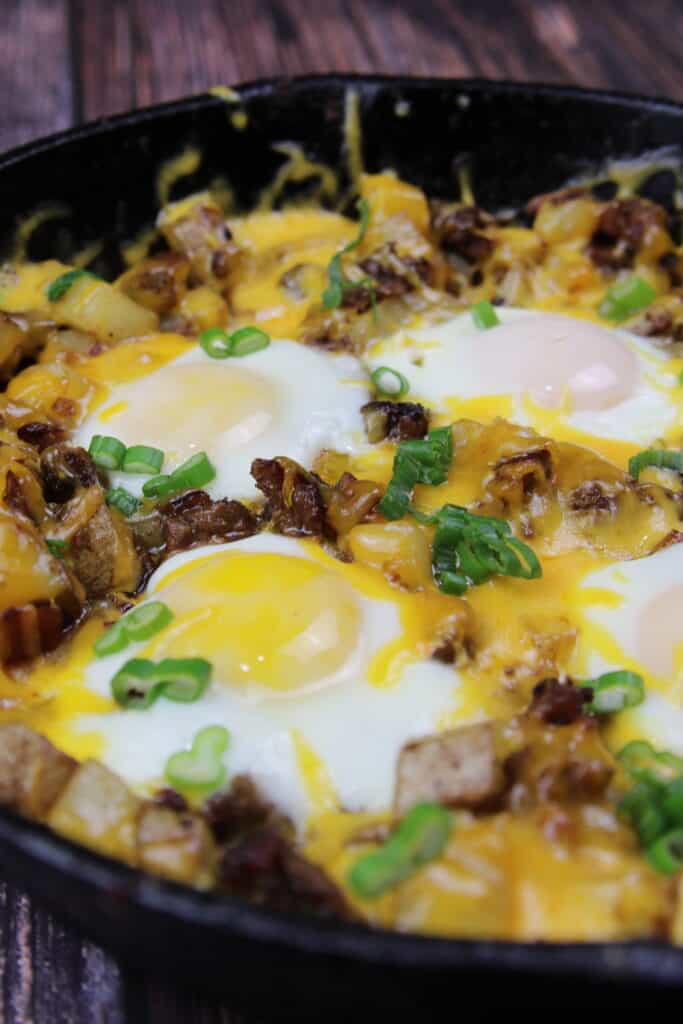 Breakfast Hash with melted cheese, over easy eggs, and potatoes in a skillet