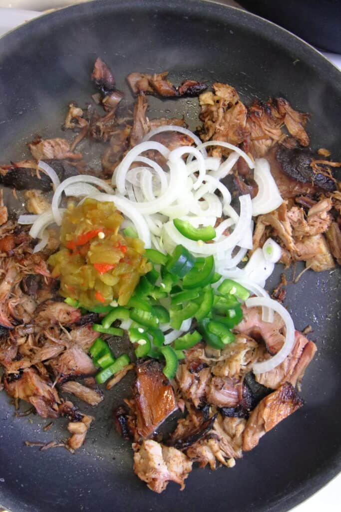 Pulled pork, peppers, onions, and green chile in a pan.