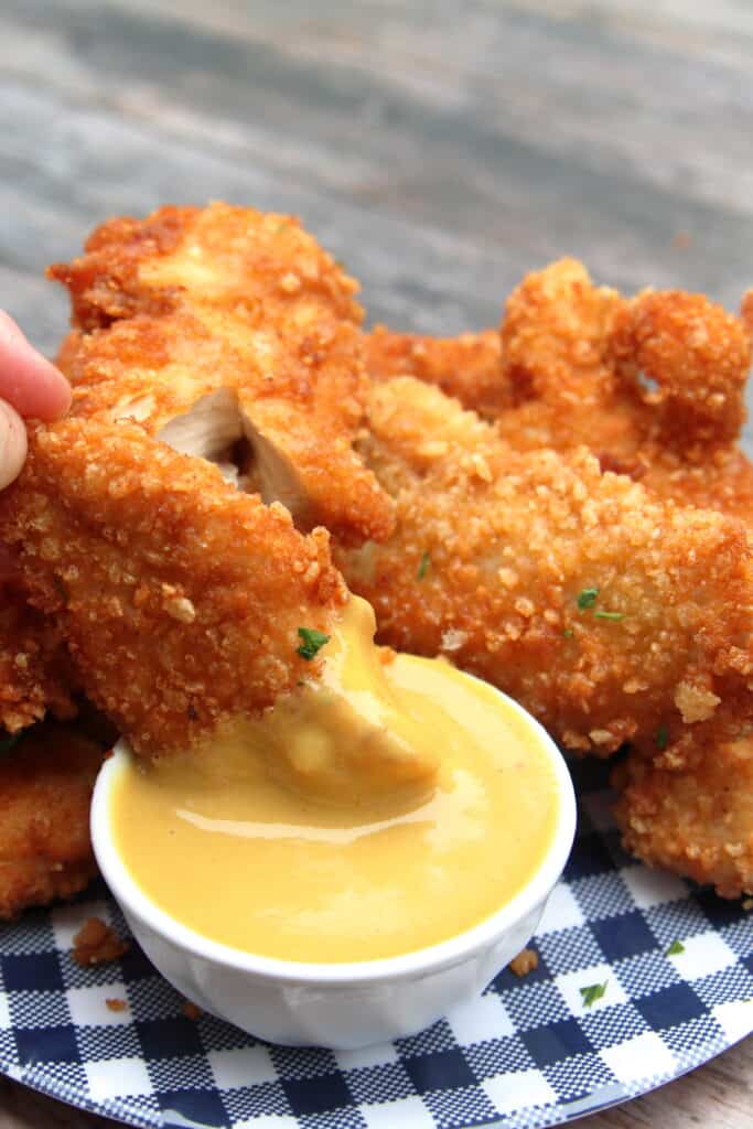 cooked chicken tenders being dipped in honey dijon sauce