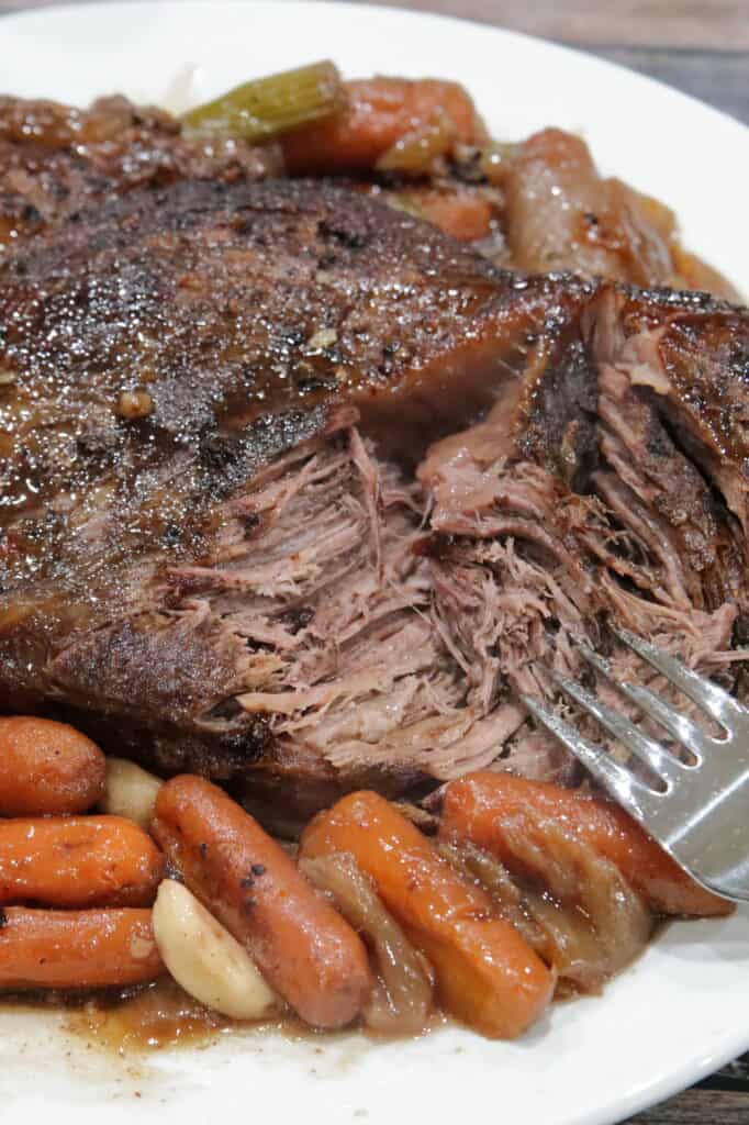 plate of chuck roast on cooked veggies with a fork tearing apart the tender meat