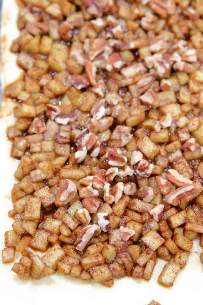 Spiced diced apples spread on a crescent roll topped with pecans
