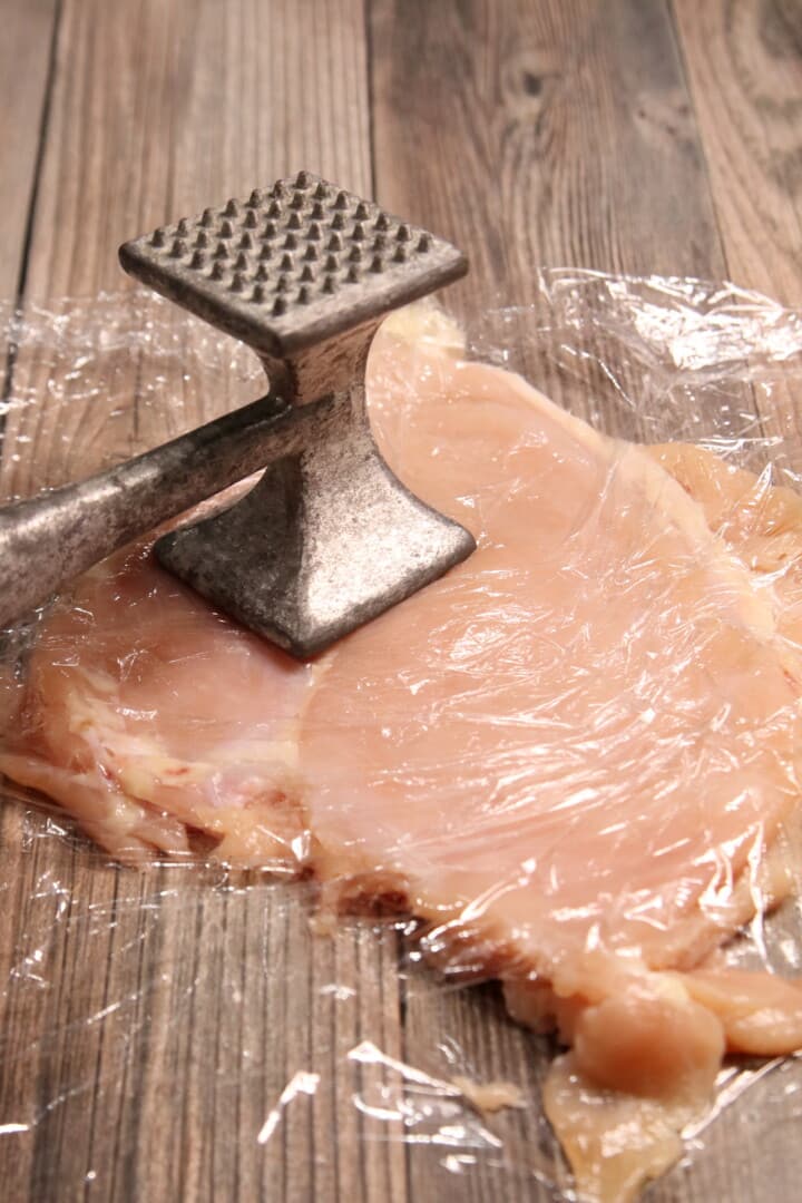 Chicken Breast between 2 pieces of plastic wrap being hammered with a meat tenderizer