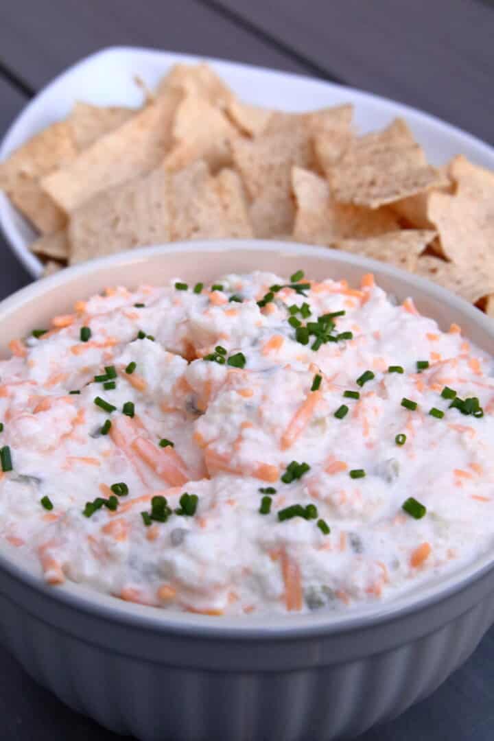 bowl of cheddar and cream cheese onion dip with chips behind it