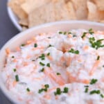 Bowl of cheddar and cream cheese onion dip with tortilla chips behind it