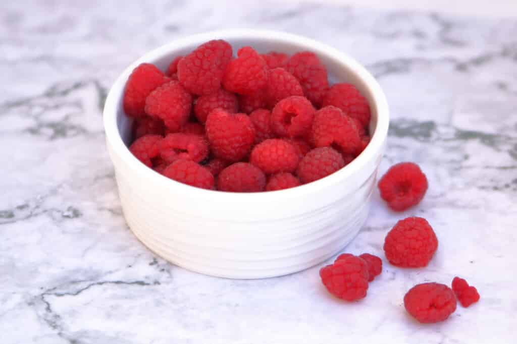 fresh raspberries in a white bowl on a white and grey marble table