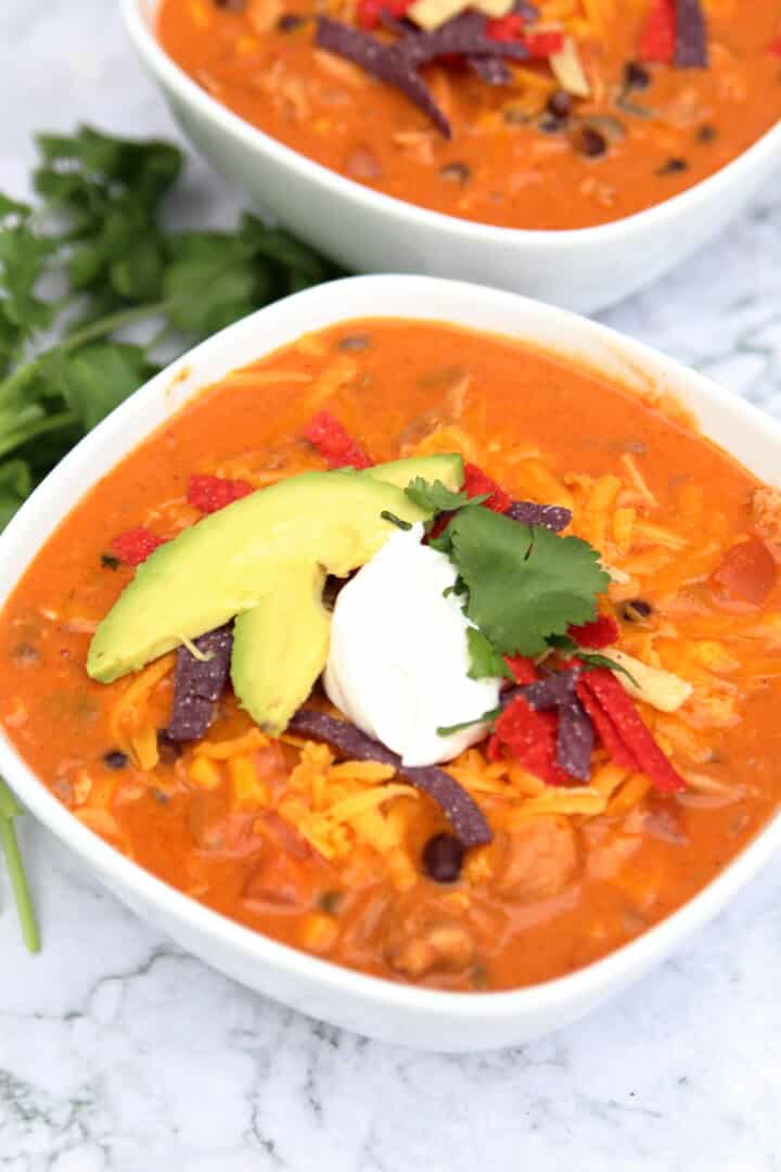 bowl of chicken enchilada soup with avocado, sour cream, cilantro, cheese, and tortilla strips on top