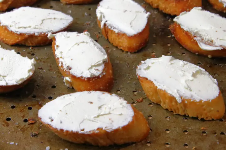 Crostini on a baking pan with goat cheese spread on top