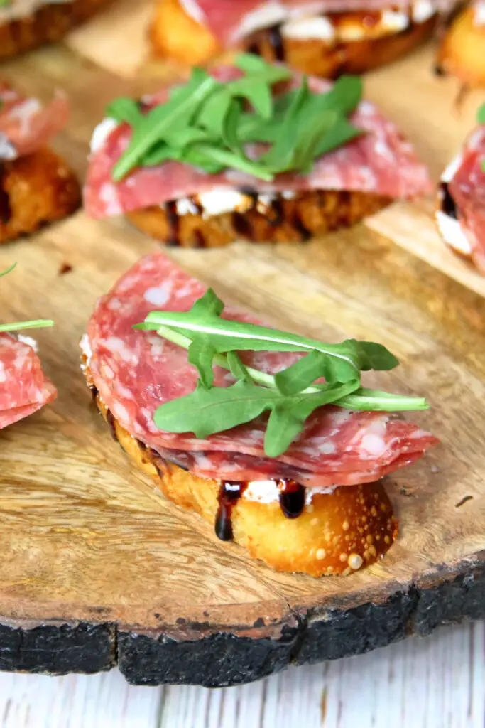 goat cheese crostini topped with arugula on a wooden platter