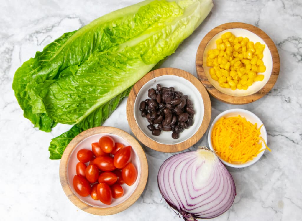 Toppings for southwest chicken salad: lettuce, cherry tomatoes, red onion, black beans, shredded cheddar, sweet corn
