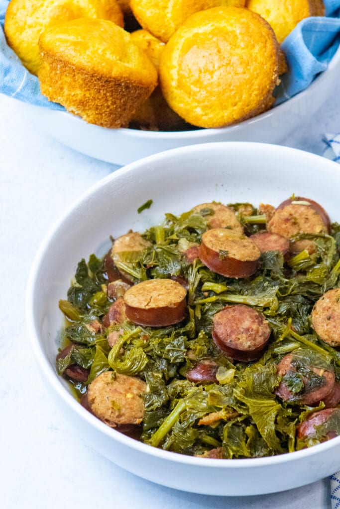 bowl of mustard greens and sausage next to a bowl of cornbread.